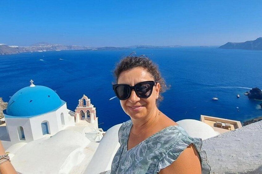 A person taking a selfie with a view of the sea and a white building with a blue dome. 5