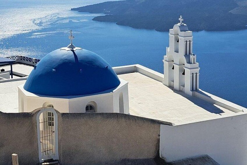 A white church with a blue dome and a bell tower overlooking a body of water. 2
