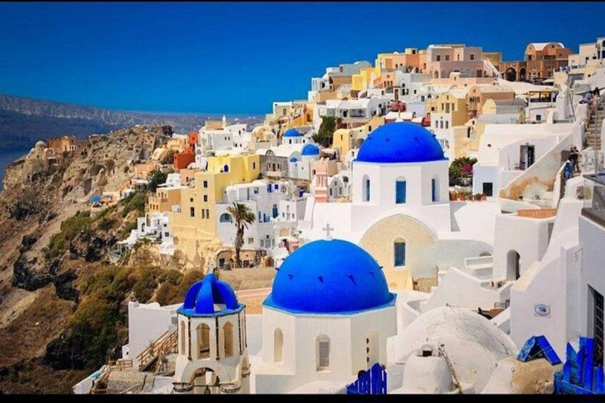 Un village côtier aux bâtiments blancs et aux dômes bleus, qui se détache sur un ciel d’un bleu limpide et un paysage rocheux. 1