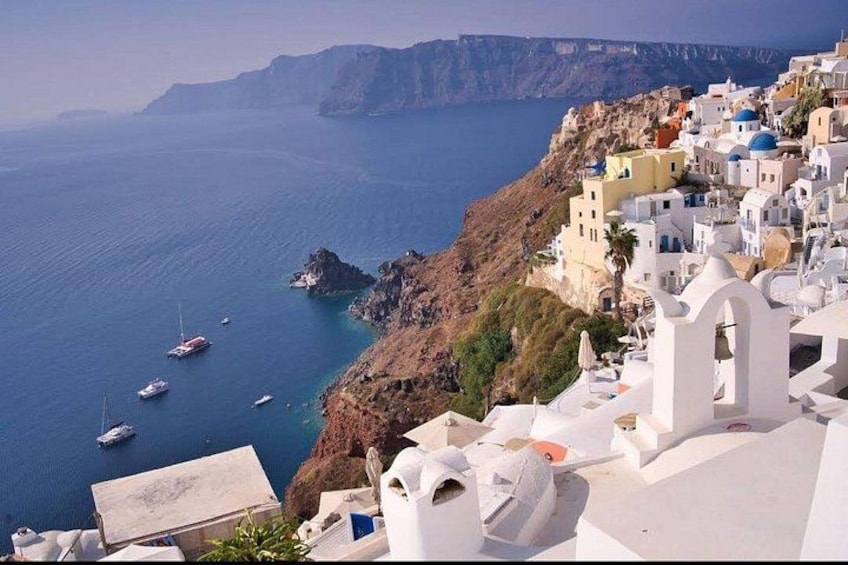 A coastal village with white buildings, a rocky cliff, and boats in the water. 4