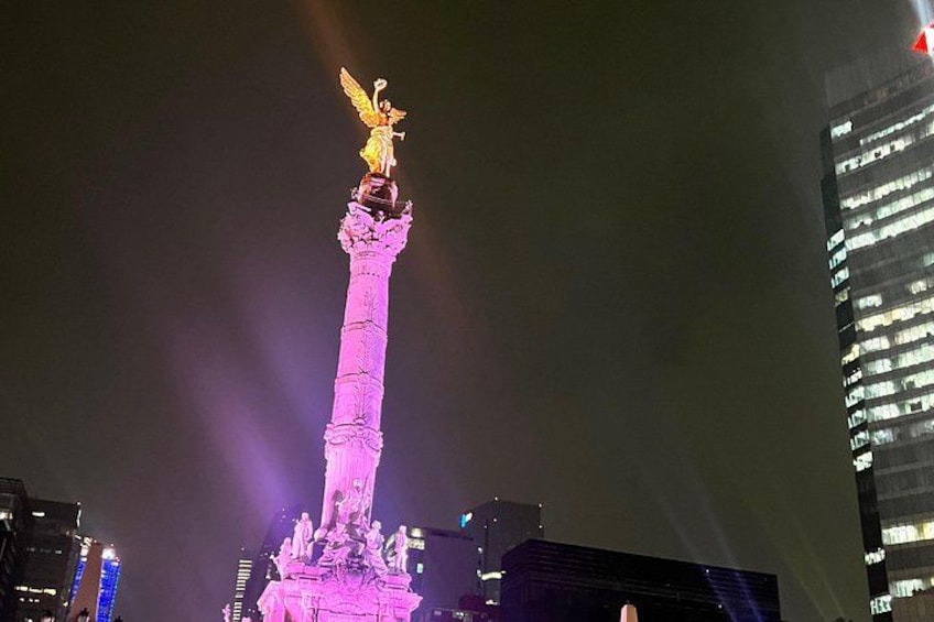 A tall monument with a golden statue on top, illuminated by purple lights. 4