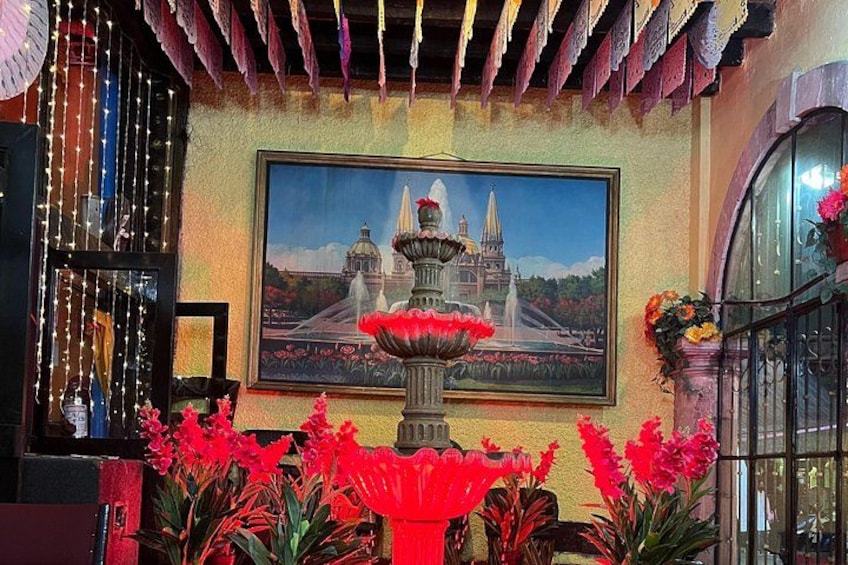 A room with a large painting of a fountain, red flowers in a vase, and a decorative ceiling. 5