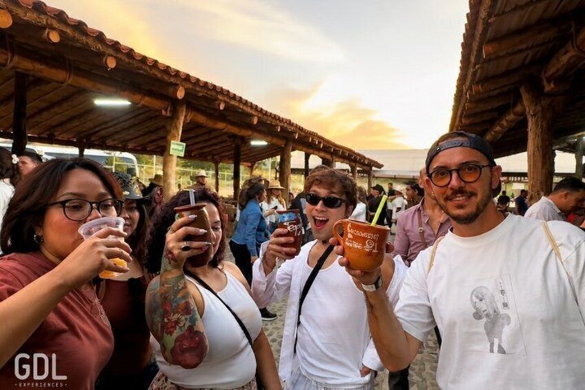Personas en un evento al aire libre con una estructura de madera, sosteniendo bebidas y un vaso con popote. 3