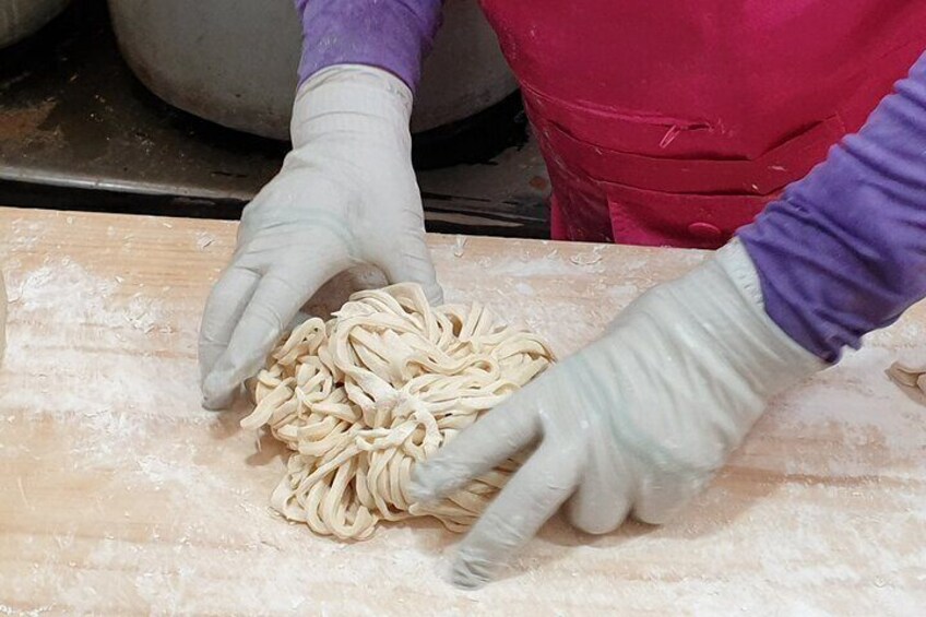 Una persona con i guanti che maneggia pasta su un piano infarinato. 3