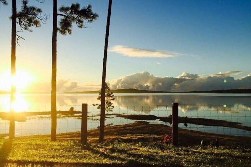 A sunrise over a calm lake with a wooden fence and trees in the foreground. 4