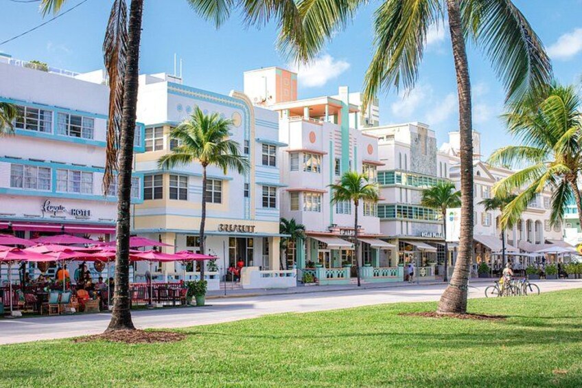 Een straat met palmbomen, een café met roze parasols en gebouwen met blauwe accenten. 4