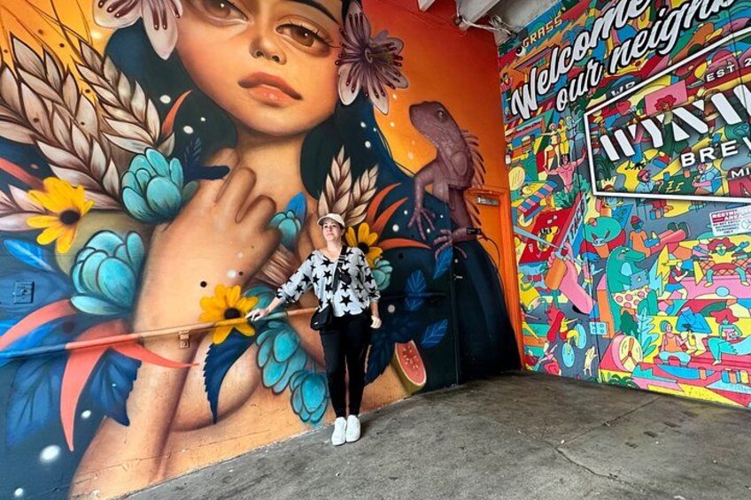 A mural with a woman standing in front of it, a colorful wall with various graphics, and a sign that says 'Welcome our neighbors.' 3