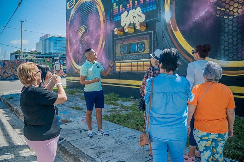 A mural with a tennis racket and ball, a person in a green shirt, and people taking photos. 2