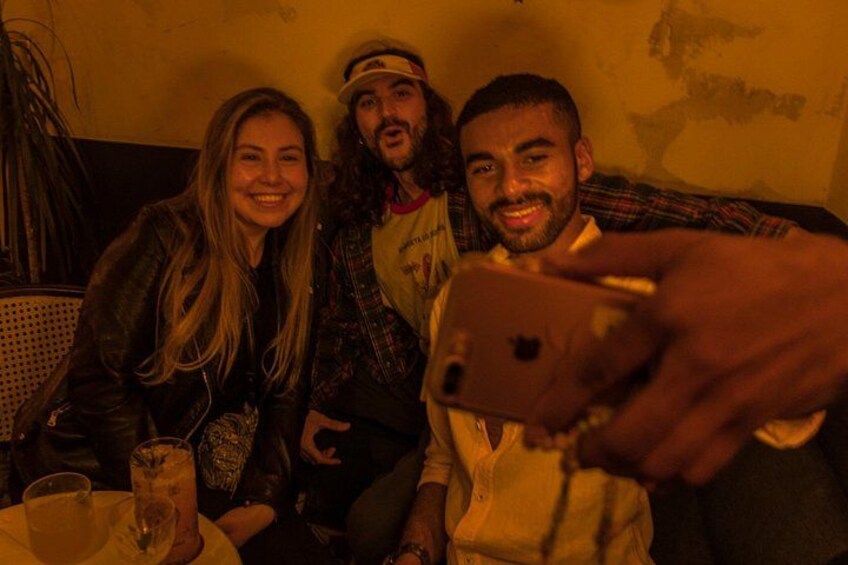 Drie personen zitten aan een tafel met drankjes, één persoon vasthoudt een smartphone. 3