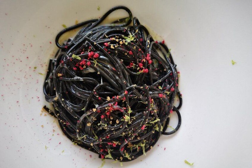 A plate of black pasta garnished with red and green herbs. 2