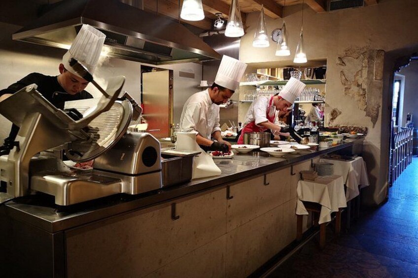 Chefs preparing food in a professional kitchen with stainless steel counters and overhead lighting. 5