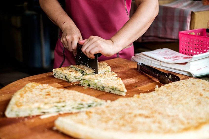 A person cutting a large pizza on a wooden board. 1