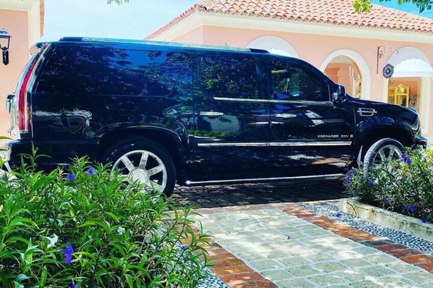 A black SUV parked in a driveway with a tiled pathway leading to a house with a pink facade and arched windows. 3