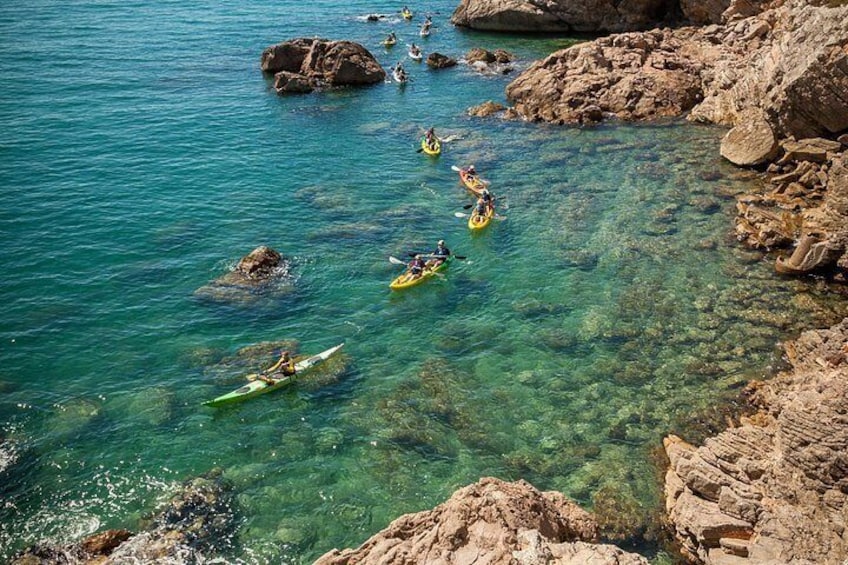 Kayakers on a clear turquoise sea with rocky shores. 1