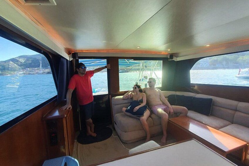 A boat interior with a sofa, a man standing by the window, and a woman sitting on the sofa. 3