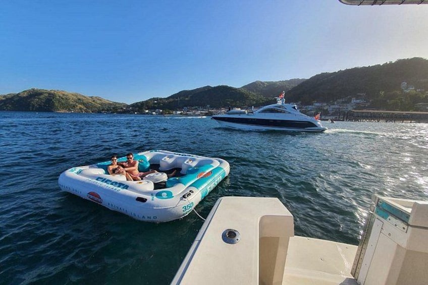 A boat with inflatable rafts on the water, a yacht in the background, and a hilly landscape. 2
