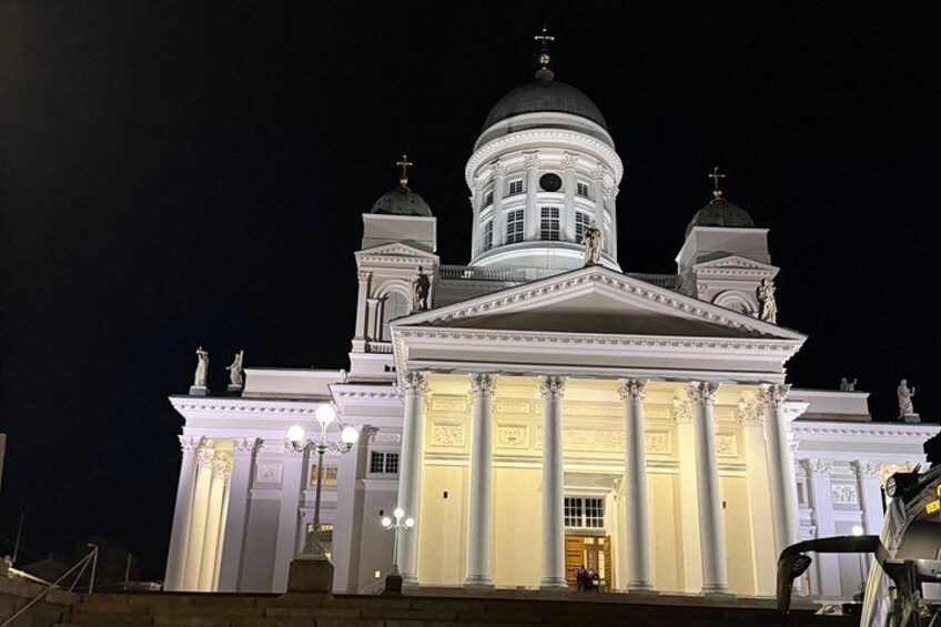 A large, illuminated church with a prominent dome and two smaller domes, columns, and statues. 2