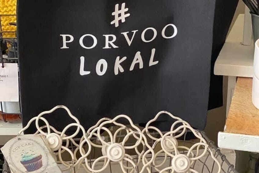 Un letrero negro con texto blanco que dice '# PORVOO LOKAL' y un estante metálico blanco con empaques para cupcakes. 3