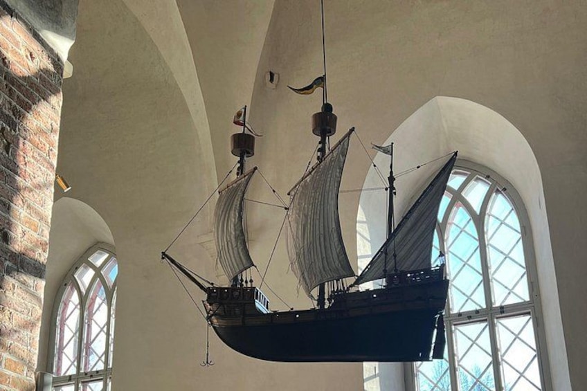 A model ship suspended from the ceiling in a building with arched windows. 2