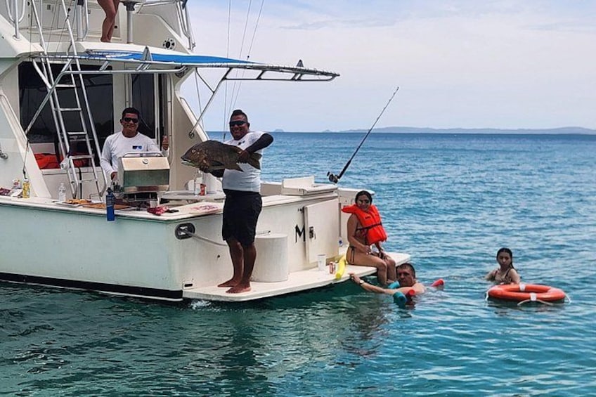 A boat with people on board, some holding a fish, and others in the water with floatation devices. 3