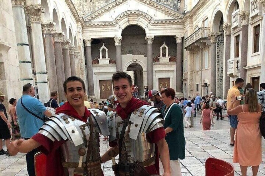 Dos personas con armadura de estilo romano posando en un edificio histórico con arcos y columnas. 2