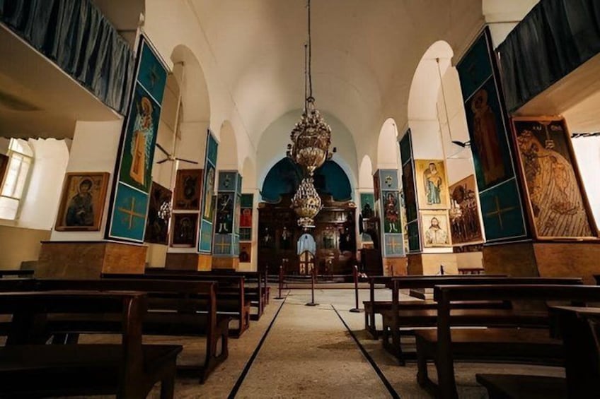 An interior of a church with wooden pews, a central altar, and religious icons on the walls. 2