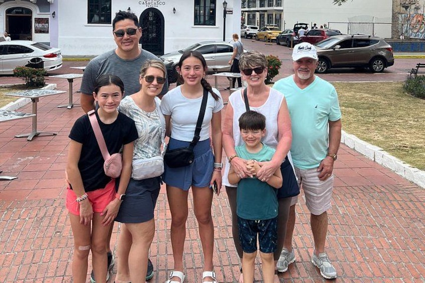 A family of seven posing in front of a building with a black door and a sign that reads 'CASA DE CORTE.' 4
