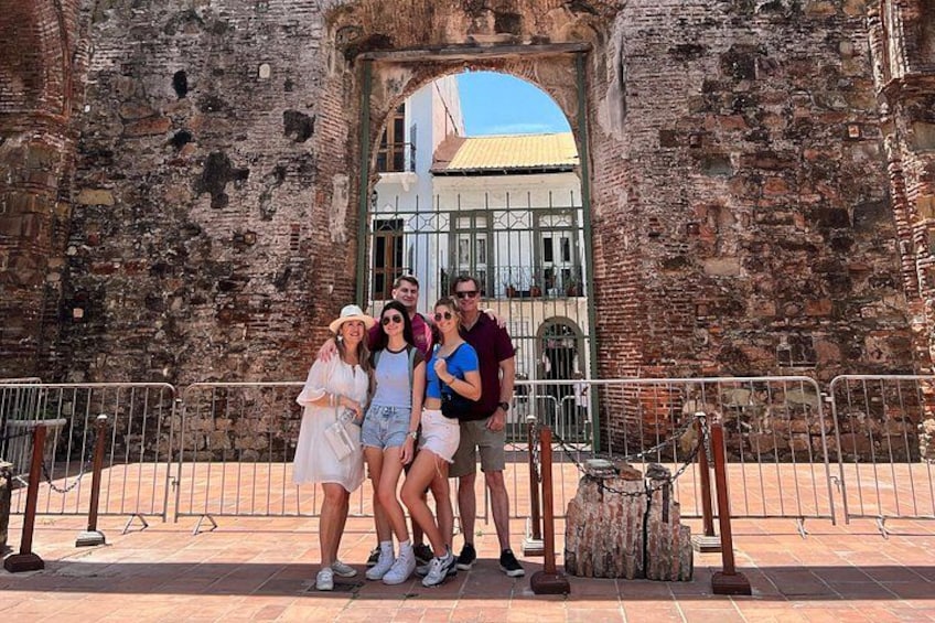 A group of people posing in front of a historic stone archway with a building in the background. 3