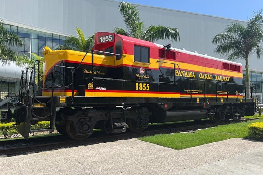 A Panama Canal Railway train numbered 1855 parked in front of a modern building. 2