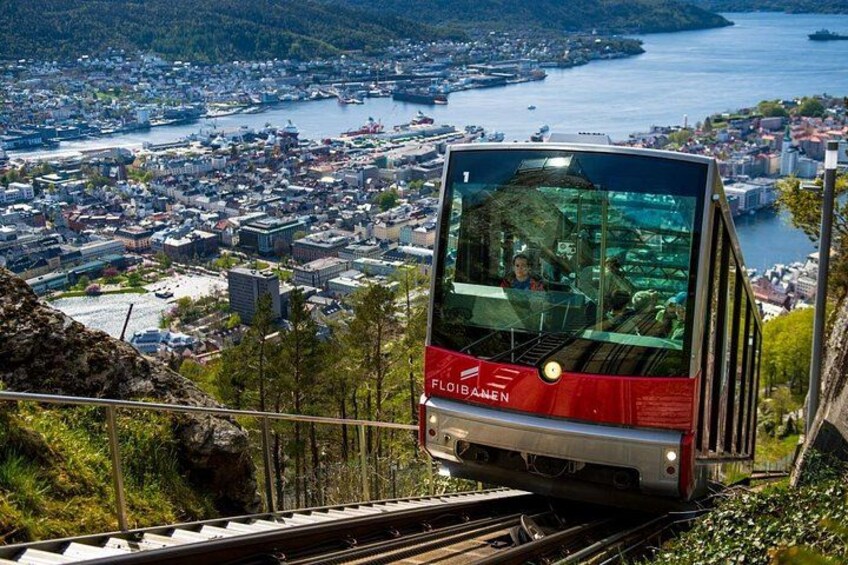 En rød kabelbane kører langs en bane med en by og et vandområde i baggrunden. 1