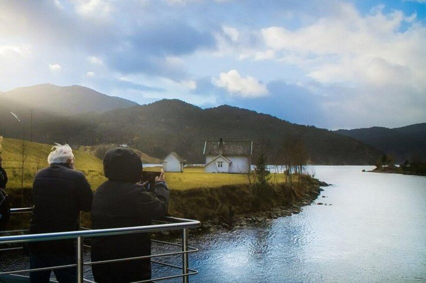 A lake with a house on the shore, a person taking a photo, and mountains in the background. 3