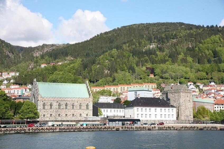 En historisk bygning med et grønt tag, et stentårn og et bjergrigt landskab i baggrunden. 2