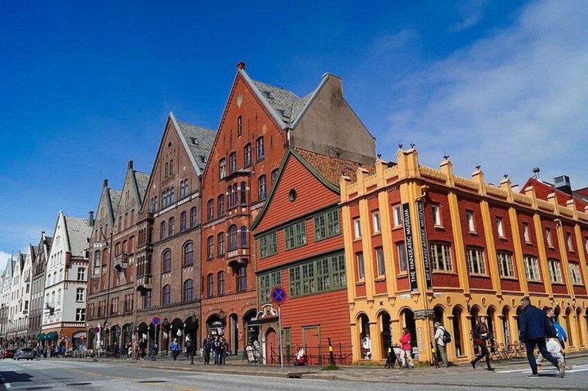 A street with historic buildings, a clear blue sky, and people walking. 2