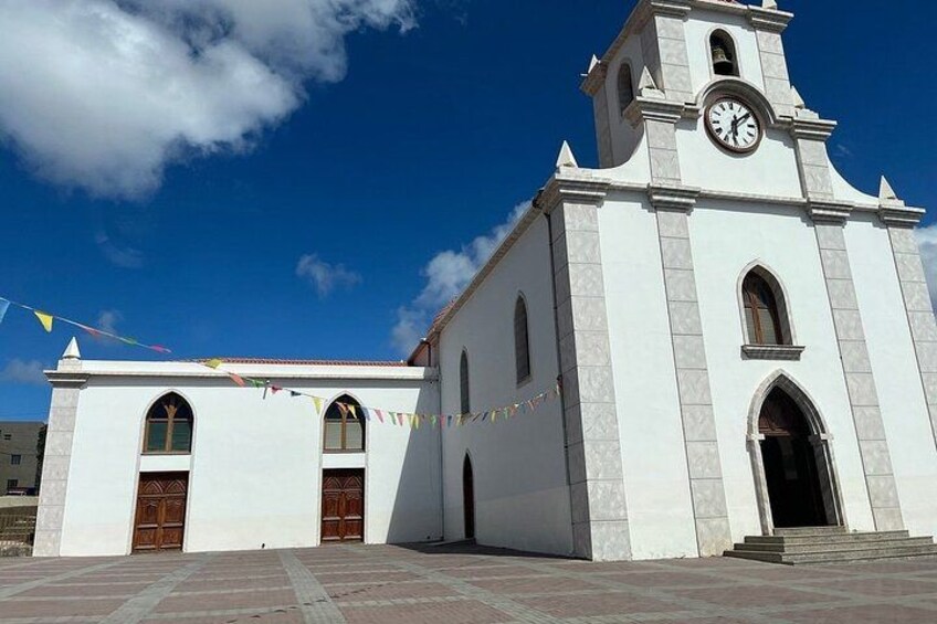 A white church with a clock tower, arched windows, and a tiled plaza. 4