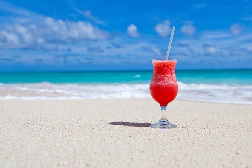 A red cocktail on a beach with a clear blue sky and turquoise ocean in the background. 2