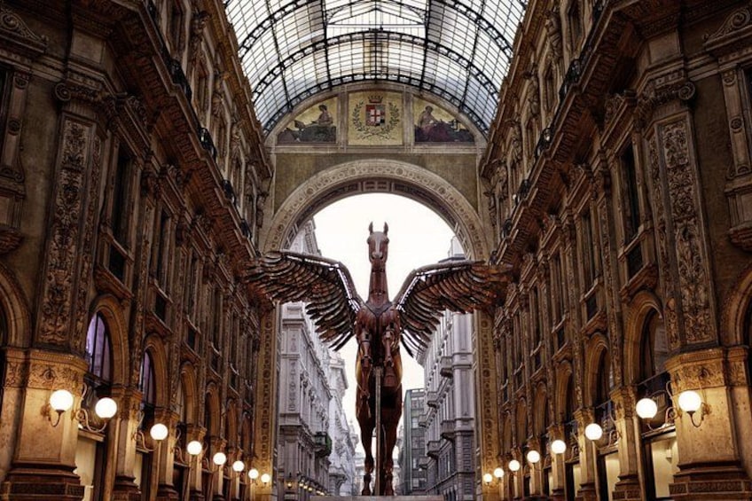 Un vaste espace intérieur d’une grande beauté architecturale, avec des colonnes richement décorées, un plafond de verre et une statue centrale. 2