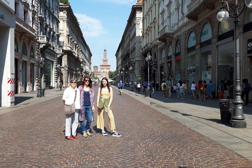 A cobblestone street lined with historic buildings, a group of people posing, and a distant clock tower. 1