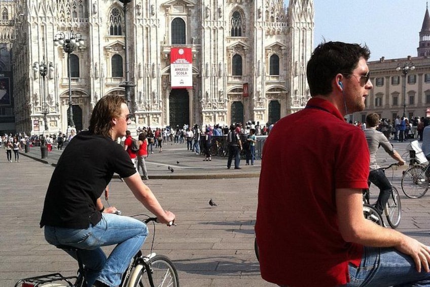 Une place animée, bordée de bâtiments historiques, où l’on voit une personne à vélo et une autre sur un scooter. 5