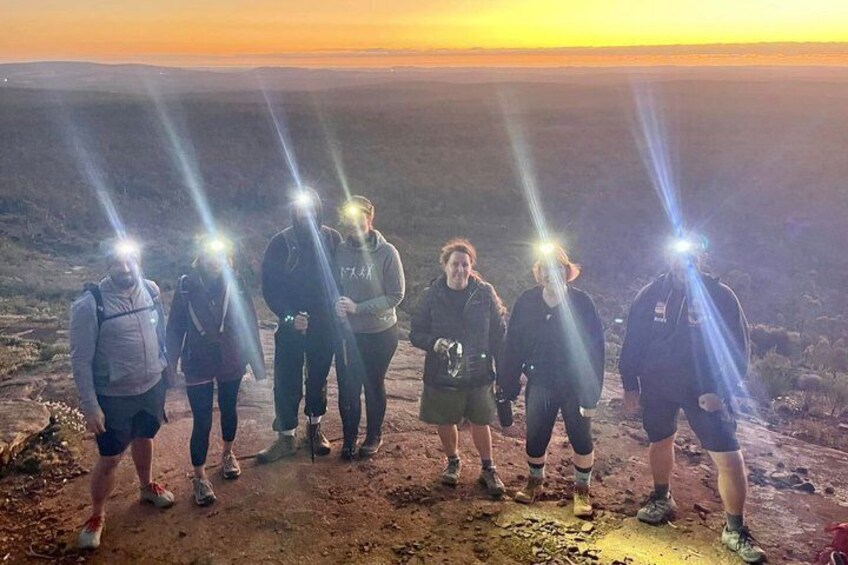 Eine Gruppe von Menschen steht auf einem Feldweg, im Hintergrund ist ein Sonnenuntergang zu sehen. 2
