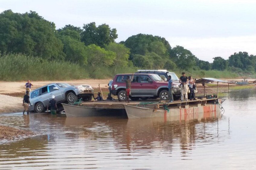 A boat carrying vehicles across a river, surrounded by greenery. 5