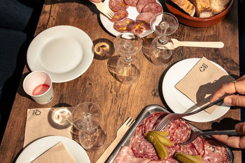Un tavolo di legno con piatti di salumi, bicchieri di vino e una ciotola di pane. 2