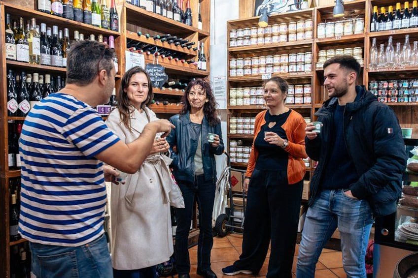 A group of people in a wine shop with shelves of wine bottles and jars. 1