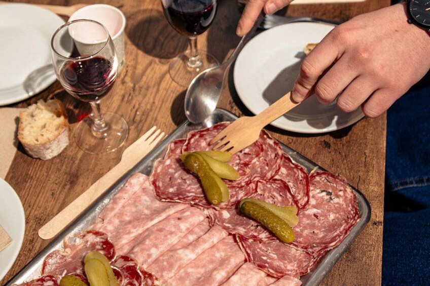 A tray of sliced meats with pickles, a fork, a spoon, and a glass of red wine on a wooden table. 5