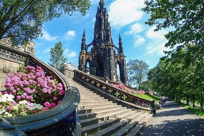 Una catedral con una aguja alta, una escalera curva y un parterre con flores rosas. 4