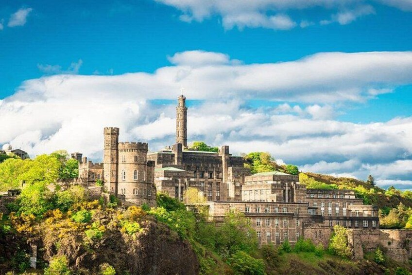A historic castle with multiple towers and a prominent central tower, surrounded by lush greenery and a clear blue sky. 3