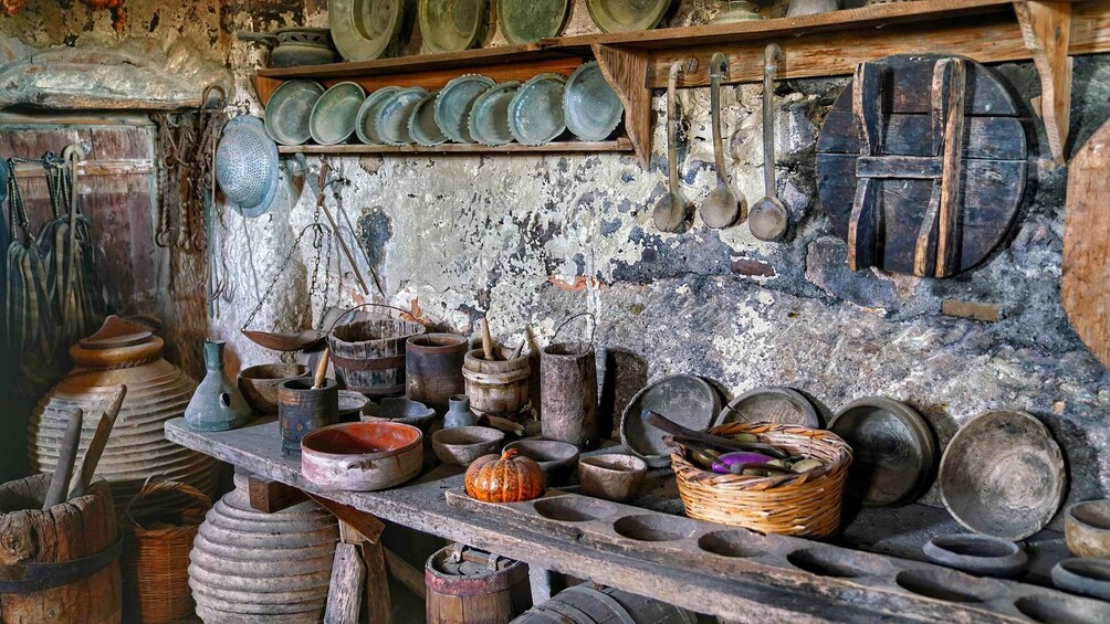 A rustic kitchen with various utensils and cookware, including pots, pans, and a wooden spoon rack. 2