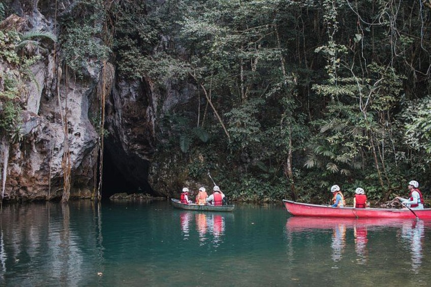 Two canoes on a calm river surrounded by dense forest and rocky cliffs. 1