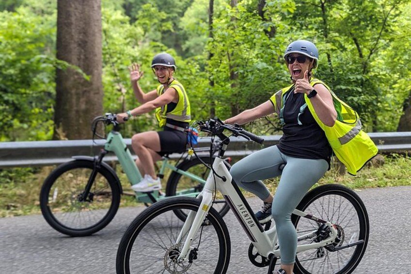 Two cyclists on a paved path surrounded by greenery. 1
