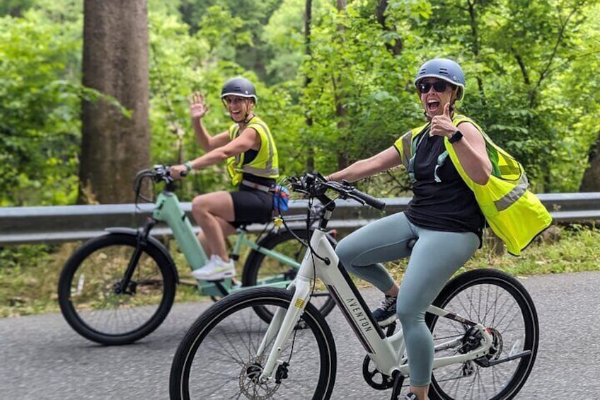 Two people riding bicycles on a paved path surrounded by greenery. 1