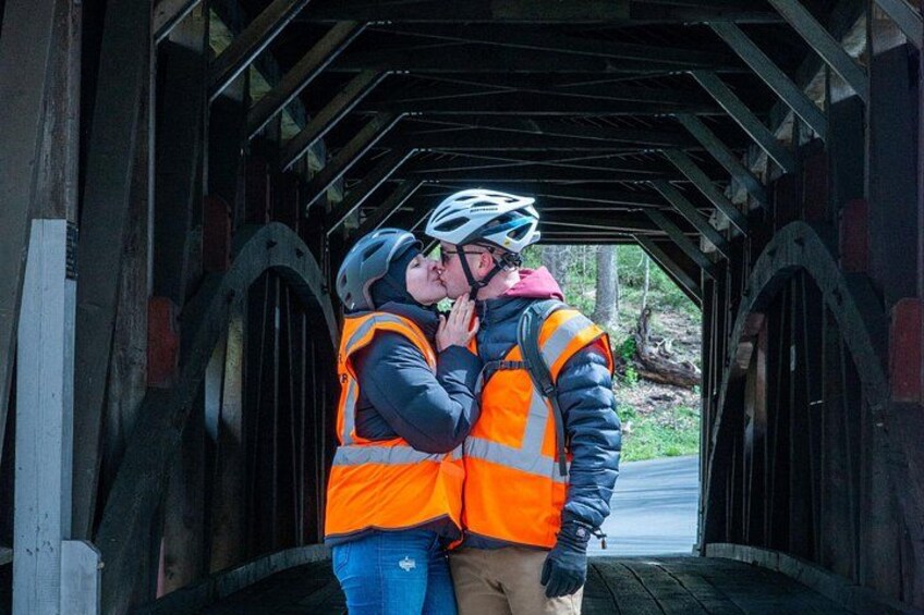 Two people wearing safety vests and helmets kissing in a covered bridge. 3